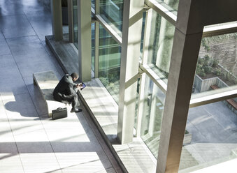 Black business man on a notebook computer sitting in a waiting area of a large open lobby. - MINF08280