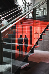 Zwei Geschäftsleute, die sich auf der Glasscheibe eines Treppenhauses eines großen Bürogebäudes spiegeln. - MINF08343
