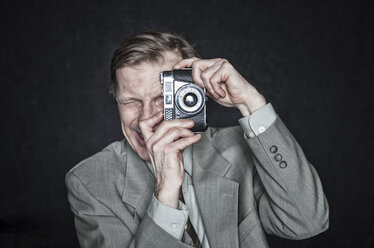 Studio-Porträt eines kaukasischen Mannes, der eine Kamera benutzt, schielt und fokussiert. - MINF08353