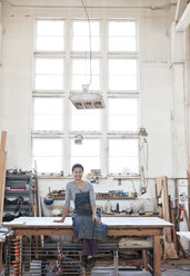 View of a smiling black woman factory worker at her work station in a woodworking factory. - MINF08375