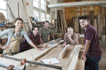 Ein Team von Fabrikarbeitern verschiedener Rassen steht neben einer Arbeitsstation in einer großen Holzverarbeitungsfabrik. - MINF08378