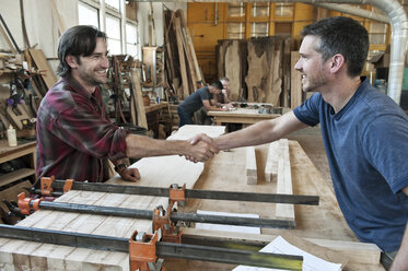 Team of four men, factory workers at a work station in a large woodworking factory, two shaking hands. - MINF08380