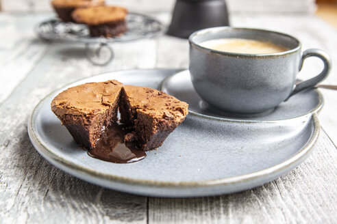 Chocolate muffin with liquid chocolate on plate with coffee cup - SARF03894