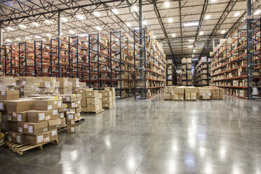 View down aisles of racks holding cardboard boxes of product on pallets in a large distribution warehouse - MINF08381