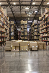 View down aisles of racks holding cardboard boxes of product on pallets in a large distribution warehouse - MINF08382