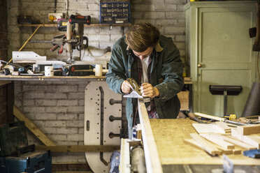 Mann arbeitet stehend an einer Werkbank in einer Holzbearbeitungswerkstatt, mit Hobel auf Holzbrett. - MINF08406