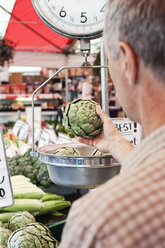 Over the shoulder view of man weighing artichoke at a fruit and vegetable market. - MINF08421