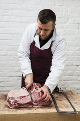 Man wearing apron standing at a wooden butcher's block, butchering piece of pork loin. - MINF08428