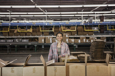 Porträt einer afroamerikanischen Lagerarbeiterin in einem großen Auslieferungslager mit in Pappkartons gelagerten Produkten. - MINF08437