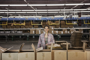 Portrait of an African American female warehouse worker in a large distribution warehouse with products stored in cardboard boxes. - MINF08437