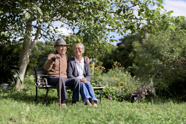 Ehepaar, älterer Mann mit Hut und Frau, die nebeneinander auf einer Bank in einem Garten sitzen. - MINF08450