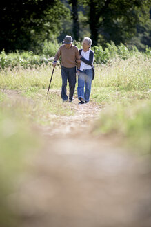 Husband and wife, elderly man wearing hat and using walking stick and elderly woman walking along path. - MINF08452