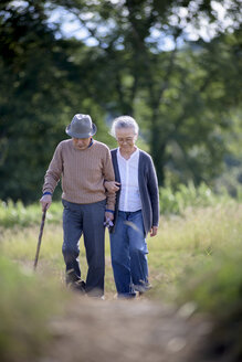 Husband and wife, elderly man wearing hat and using walking stick and elderly woman walking along path. - MINF08453