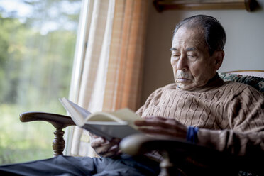 Elderly man sitting in rocking chair by a window, reading book. - MINF08461