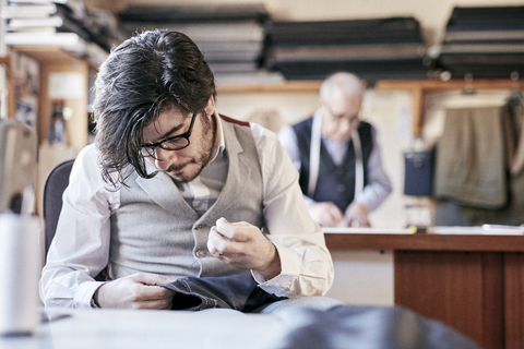 Schneiderin mit Maßband um den Hals bei der Arbeit mit Stoff an der Werkbank, lizenzfreies Stockfoto