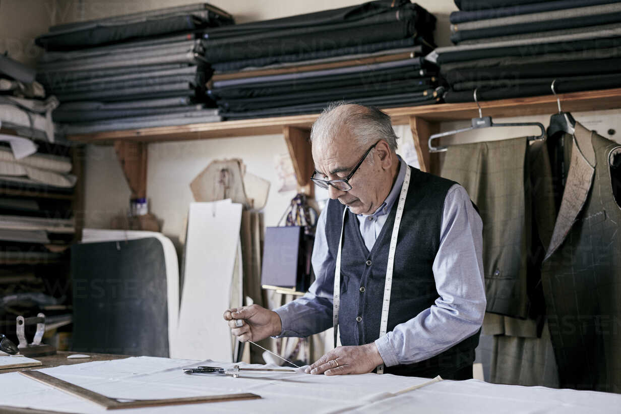 https://us.images.westend61.de/0001023097pw/tailor-with-measuring-tape-around-neck-working-with-material-at-bench-MINF08487.jpg