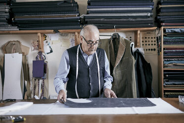 Tailor with measuring tape around neck working on a cut piece of fabric. - MINF08488