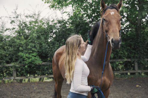 Eine junge Frau und ein braunes Vollblut-Rennpferd auf einer Koppel - MINF08525