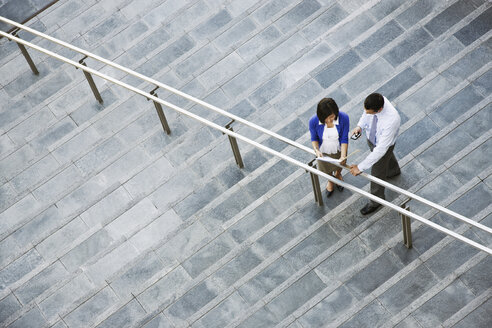 Blick von oben auf eine Geschäftsfrau und einen Geschäftsmann, die auf den Stufen zu einem großen Bürogebäude stehen. - MINF08551