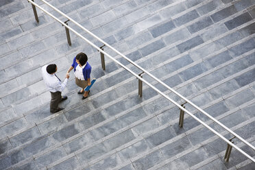 Blick von oben auf eine Geschäftsfrau und einen Geschäftsmann, die auf den Stufen zu einem großen Bürogebäude stehen. - MINF08552