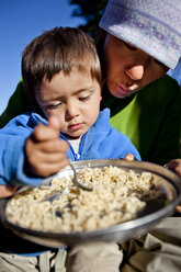 Ein Junge sitzt auf dem Schoß seiner Mutter und isst Nudeln, während sie am Squaw Pass campen. - AURF00156