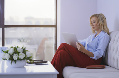 Blonde Frau sitzt auf der Couch und benutzt einen Laptop - AZF00074