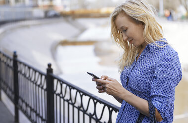 Blond woman using smartphone on a street - AZF00081