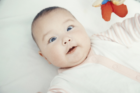 Lächelndes Baby auf dem Bett liegend, Porträt, lizenzfreies Stockfoto