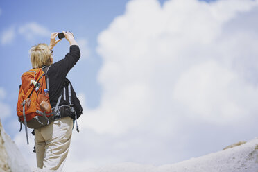 Touristin mit Rucksack, die mit ihrem Smartphone Fotos von Wolken macht - AZF00090
