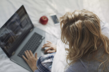 Frau sitzt auf dem Bett und benutzt einen Laptop - AZF00093