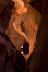 Eine Frau wandert durch den Antelope Canyon in Arizona inmitten von Sonnenlicht und roten Felsen. - AURF00160