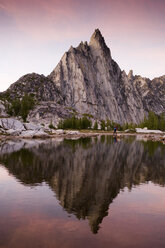 Eine Frau wandert bei Sonnenuntergang in der Nähe von Bergziegen an einem See unterhalb des Prussik Peak, Alpine Lakes Wilderness, Leavenworth, Washington. - AURF00167