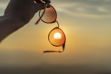 Hand holding sunglasses against sunset - AFVF01380