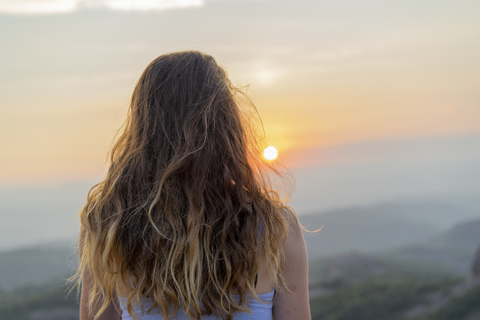 Frau beobachtet Sonnenuntergang in den Bergen, lizenzfreies Stockfoto
