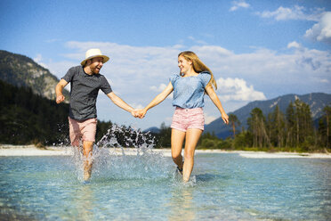 Young couple holding hands and running through water - MAEF12704