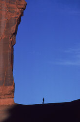 A man is dwarfed by a towering stone cliff, Utah, USA. - AURF00189