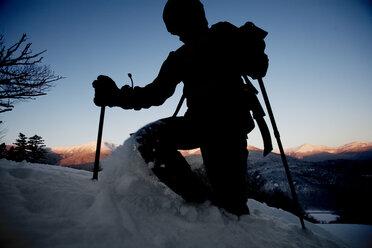 Ein Mann wandert durch den Tiefschnee auf dem Mt. Washington, die Silhouette hebt sich von der untergehenden Sonne ab. - AURF00194