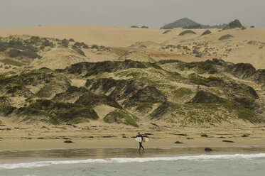 Ein Mann in einem Neoprenanzug läuft mit einem Surfbrett am Strand in der Nähe von Pichidangui, Chile. - AURF00220