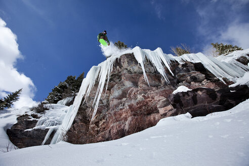 Ein männlicher Snowboarder springt an einem sonnigen Tag in Colorado von einer Eiswasserfallklippe. - AURF00235