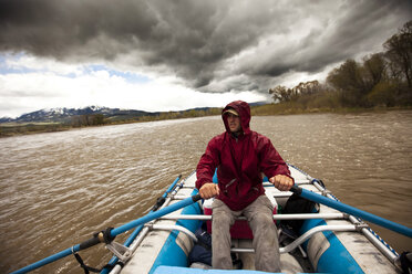 Ein Mann flößt unter stürmischem Himmel in Montana einen Fluss hinunter. - AURF00257