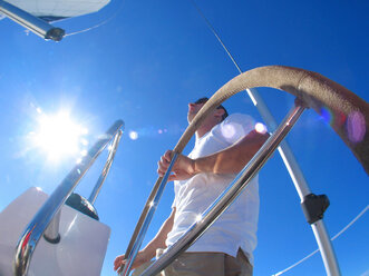 A skipper steering on board a yacht under blue skies while cruising in Pittwater on the North Shore from Sydney, Australia. - AURF00320