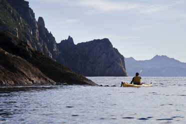 A sea kayaker paddles towards sea cliffs on Schouten Island, Freycinet National Park, Tasmania, Australia. - AURF00325