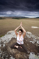 Eine Frau praktiziert Yoga auf einem Feld unter bewölktem Himmel in Brasilien. - AURF00429
