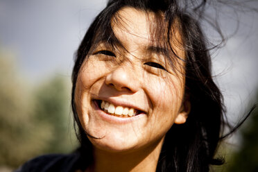 Eine Frau lächelt, während ihr Haar bei einem Heuausritt in einer Apfelplantage im Wind weht. - AURF00443
