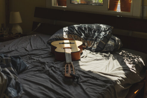Akustische Gitarre auf einem Bett mit Sonnenlicht, das durch das Fenster fällt - AFVF01396