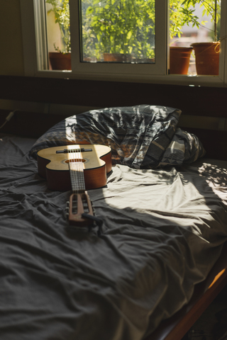 Akustische Gitarre auf einem Bett mit Sonnenlicht, das durch das Fenster fällt, lizenzfreies Stockfoto