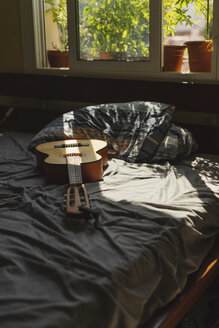 Akustische Gitarre auf einem Bett mit Sonnenlicht, das durch das Fenster fällt - AFVF01397