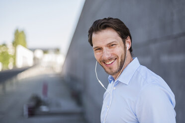 Portrait of smiling businessman wearing earbuds - DIGF04810