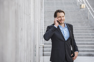 Smiling businessman at stairs talking on smartphone - DIGF04822