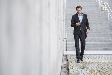 Geschäftsmann, der auf einer Treppe geht und auf sein Smartphone schaut - DIGF04823